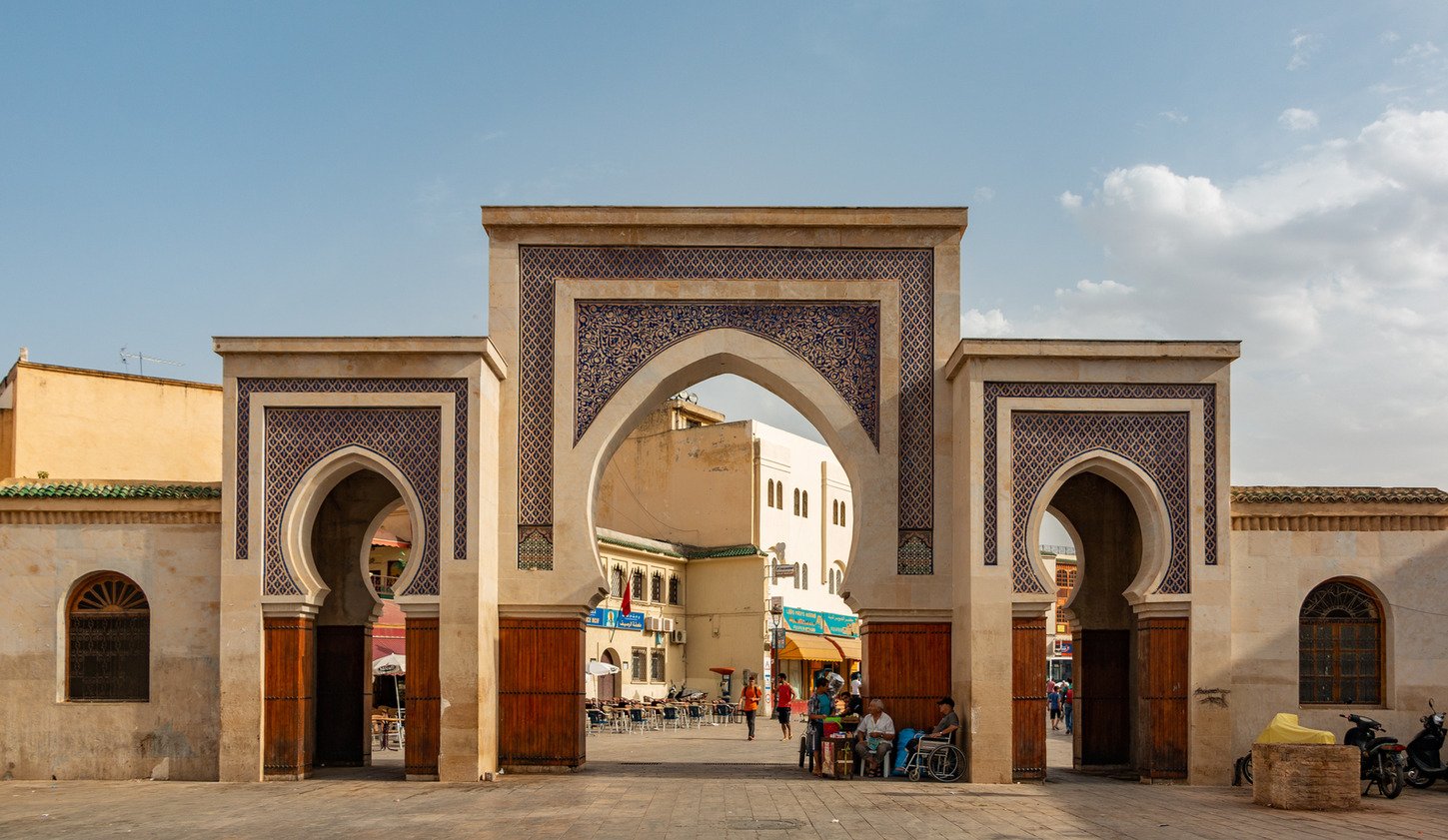 Bab Bou Jeloud gate in Fes with three horseshoe arches, blue tilework and people entering the medina