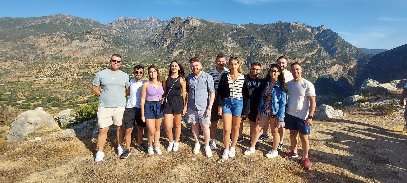 Group of travelers standing at a rocky viewpoint with rugged mountains and a green valley behind them in Morocco