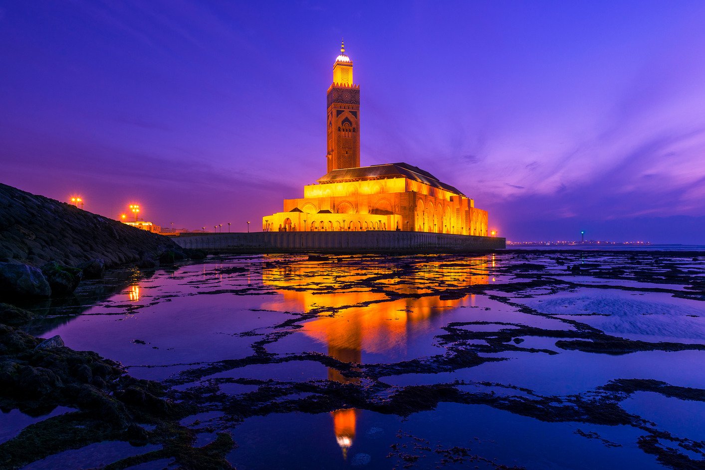 Hassan II Mosque in Casablanca glowing at night beside the Atlantic with reflections in tidal pools