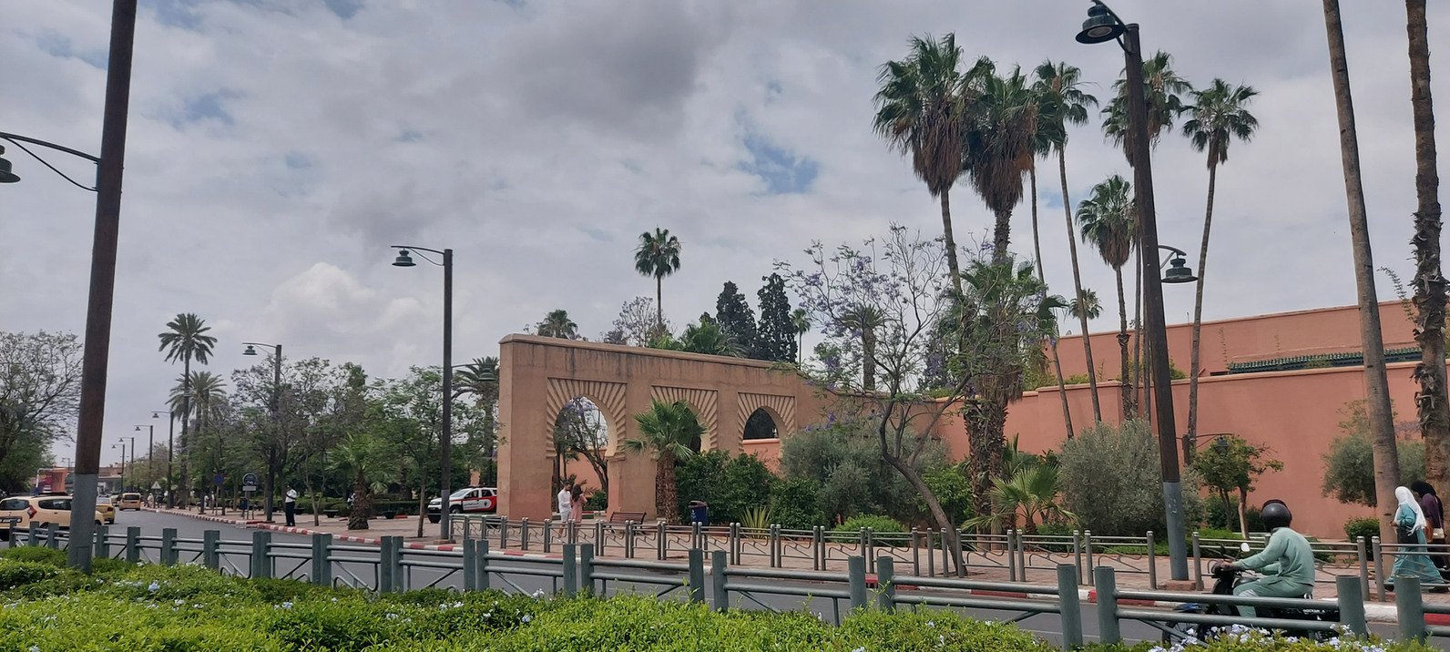 Moroccan city street beside ochre walls, arched gateways, landscaped greenery and tall palm trees