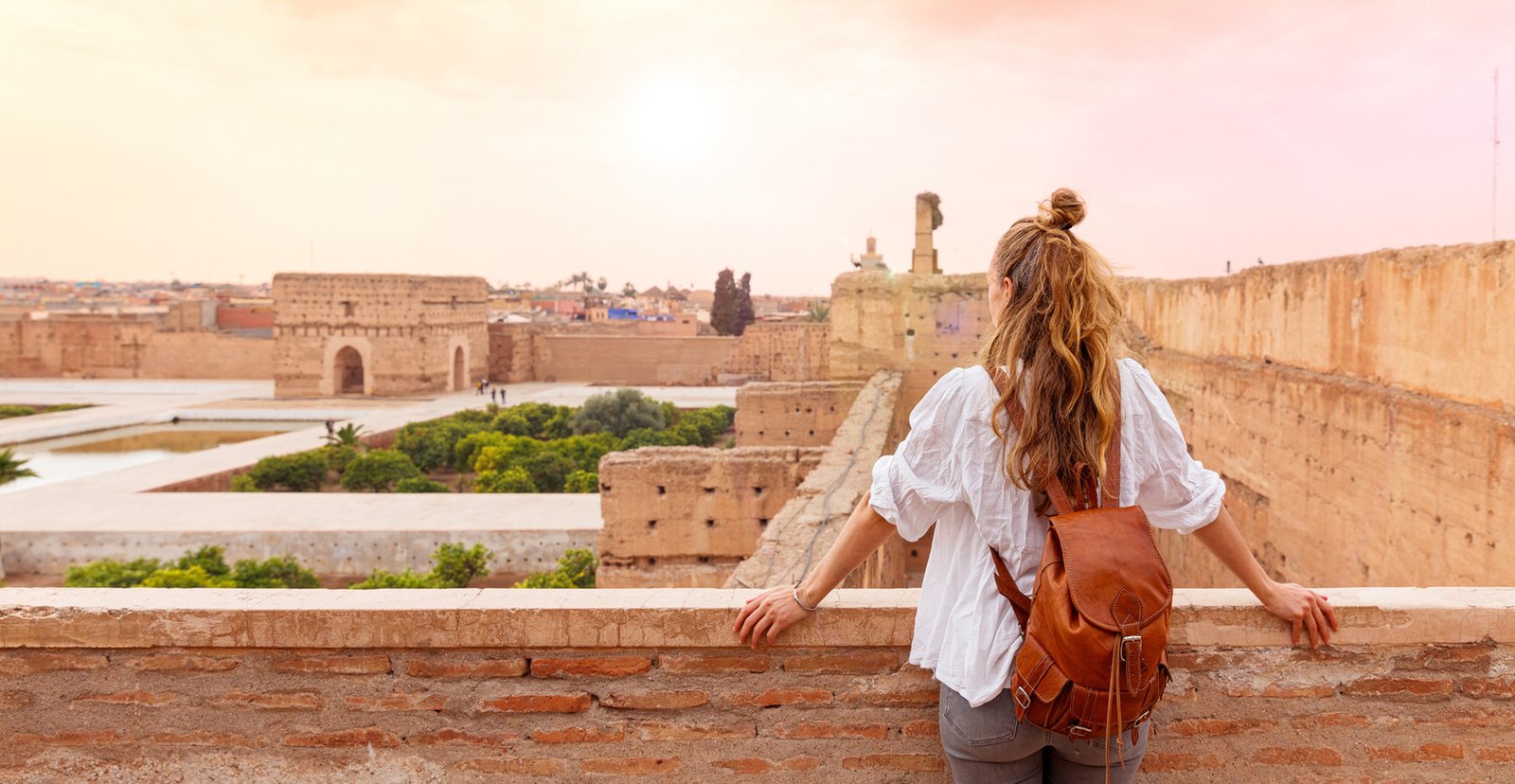 Traveler with a backpack looking across the earthen walls and courtyard ruins of El Badi Palace in Marrakech